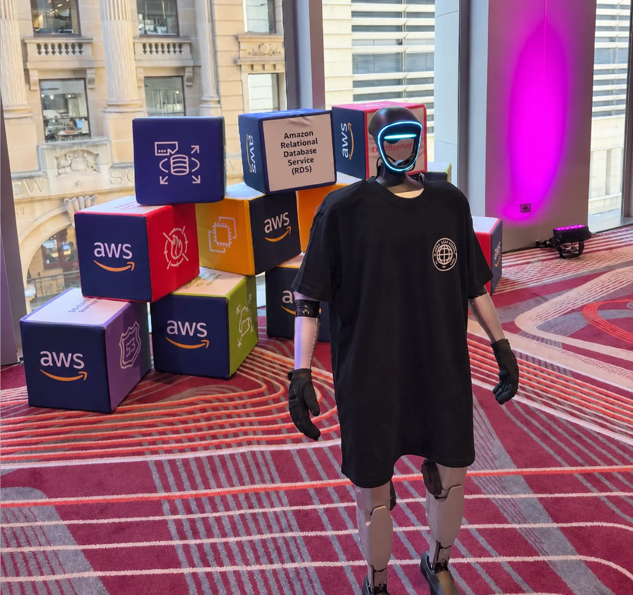 Rocco humanoid robot beside AWS service display cubes at an event
