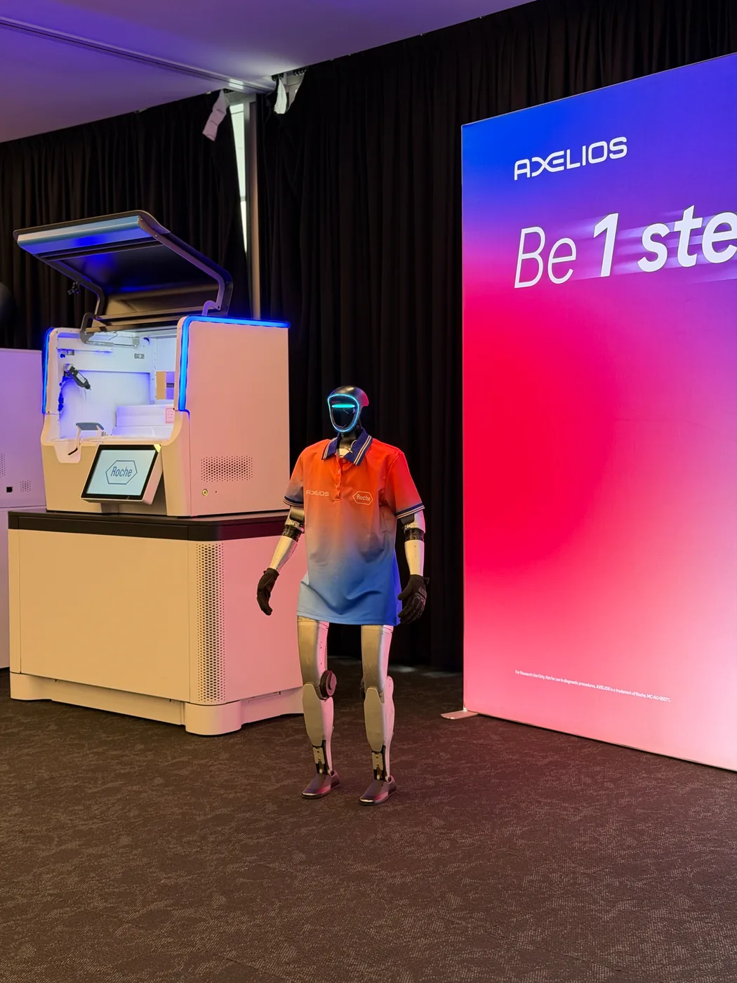 Rocco in a Roche polo beside an AXELIOS 1 sequencing instrument
